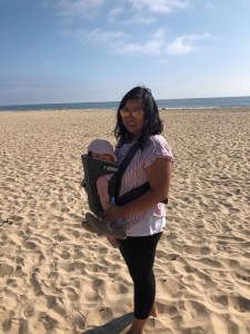 Mom on the beach with baby in carrier.